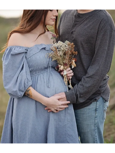 Couple embracing with hands on pregnant belly outdoors, holding dried flowers.