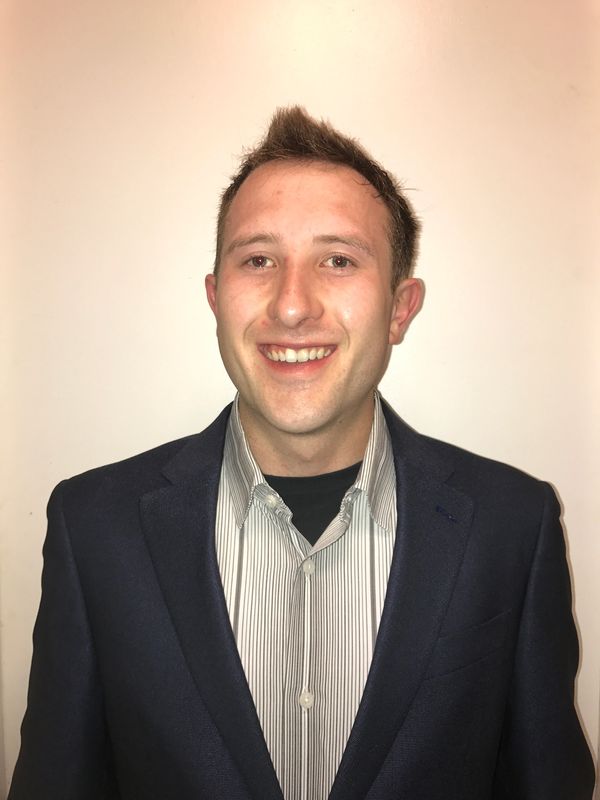 Young man in a suit jacket smiling against a plain background.