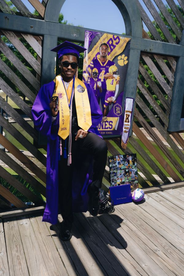 Graduate in purple gown and cap posing with sports memorabilia.
