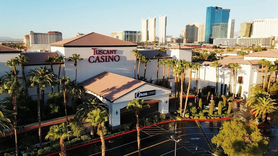 Aerial view of Tuscany Casino with palm trees and city skyline in the background.