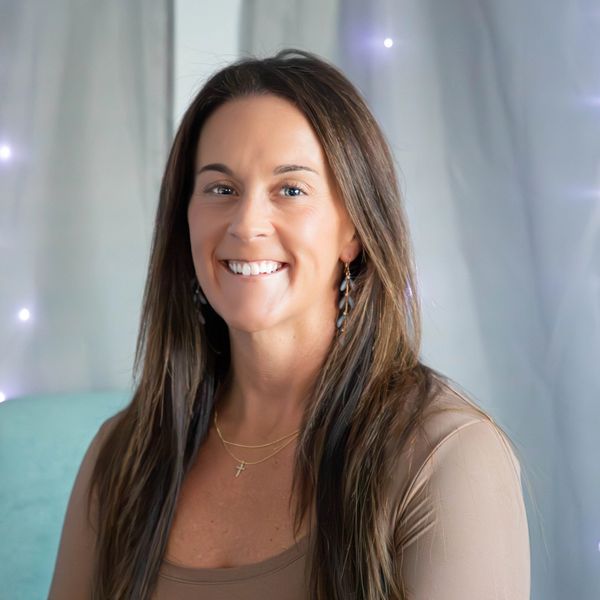 Smiling woman with long hair and earrings against a softly lit background.