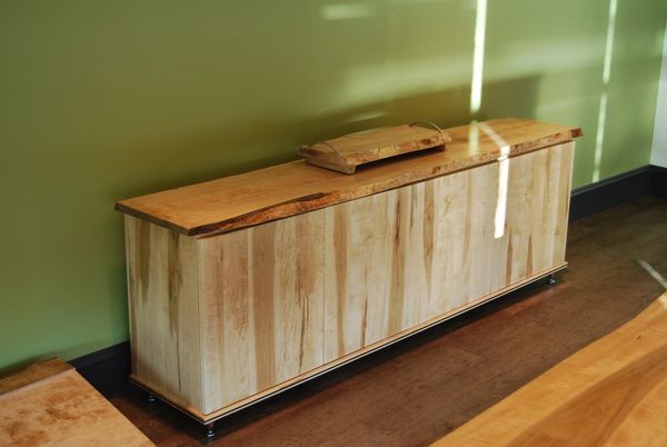 Smooth wooden sideboard with a natural finish against a green wall.