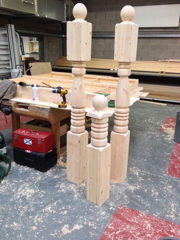 Three large, unfinished wooden balusters in a workshop.