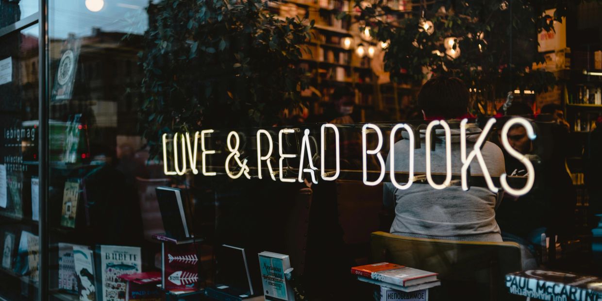 Neon sign saying 'LOVE &amp; READ BOOKS' on a bookstore window at dusk.