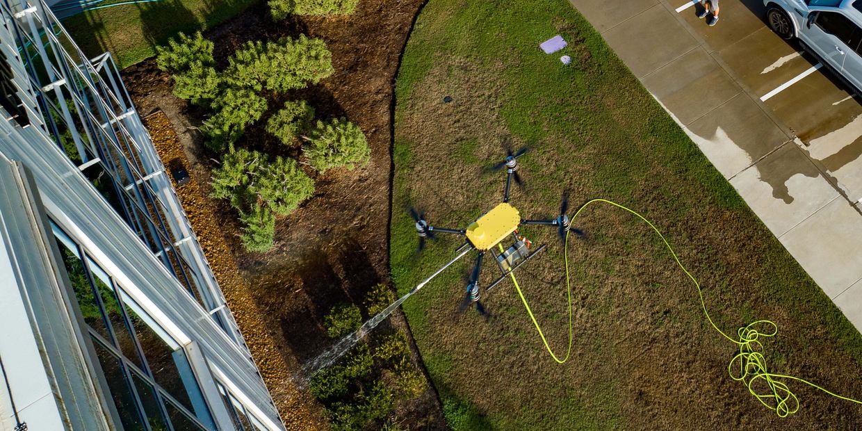 A cleaning drone hovers beside a commercial building, washing its windows with precision.