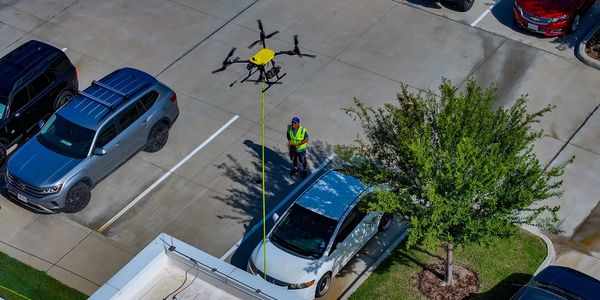 A Drone Cleaning Operator is using a drone pressure washer to clean a commercial building.