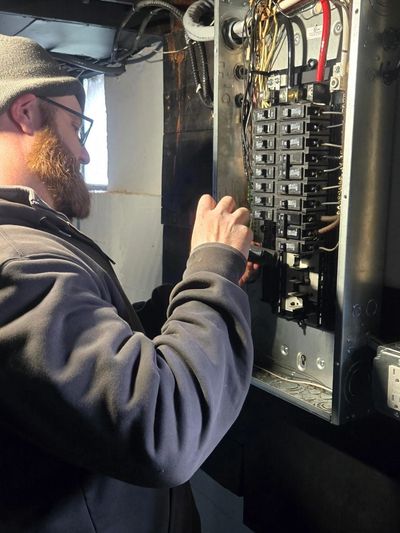 A man works on an electrical panel, adjusting circuit breakers.