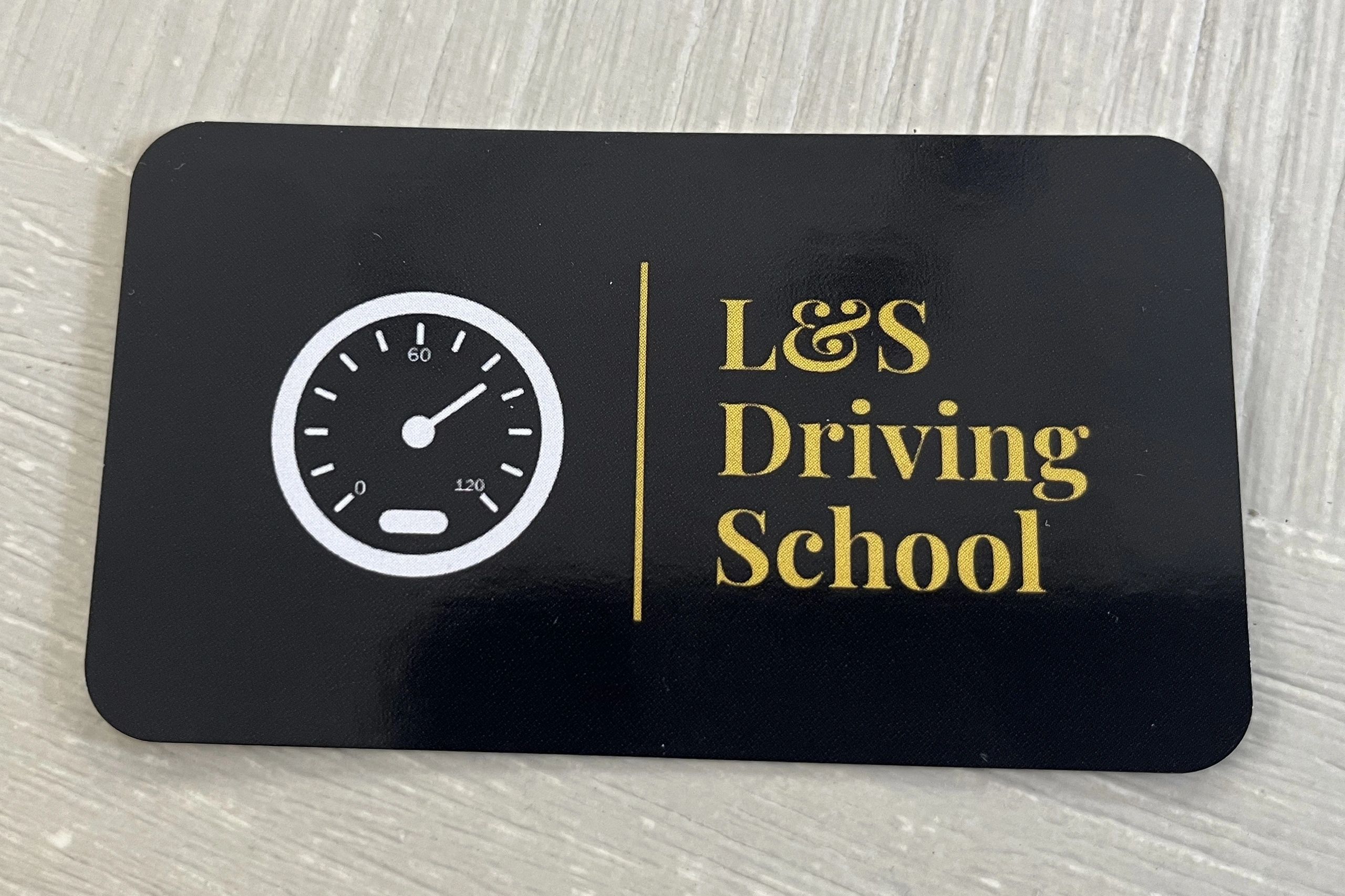 L&S Driving School business card. Black card with the business name in gold lettering.