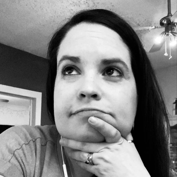 A woman in deep thought looking upward with hand on chin indoors.