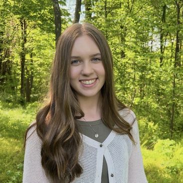 Young woman smiling outdoors in a sunlit forest.
