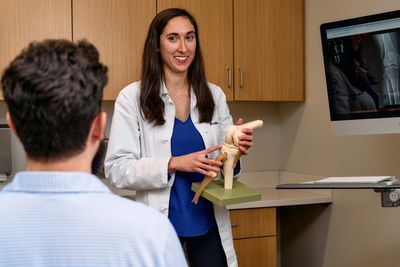 Doctor explaining knee anatomy to a patient with a knee model and X-ray images.