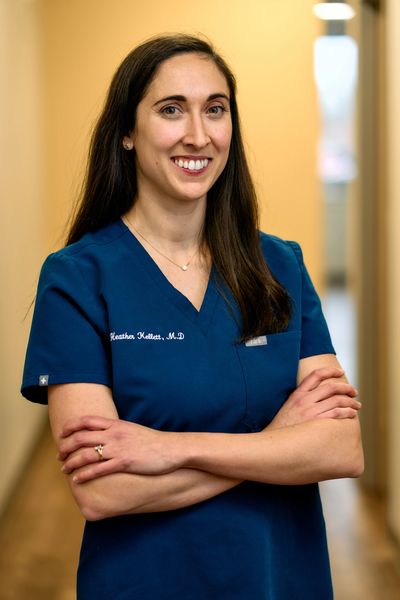 Confident female doctor in blue scrubs with arms crossed, smiling.