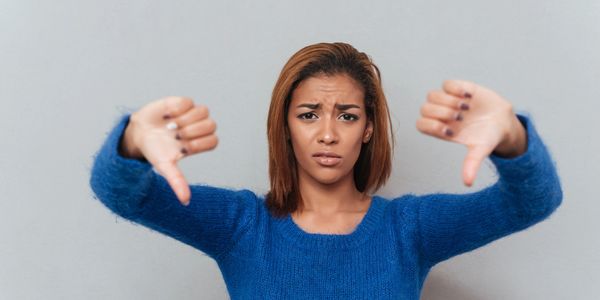 Woman in blue sweater showing thumbs down with a disappointed expression.