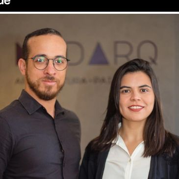 Two professionals posing in an office setting with a company logo in the background.