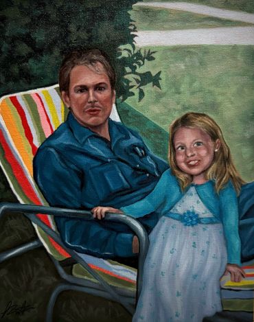 A man and young girl sit together outdoors on a striped lawn chair.
