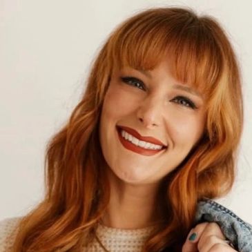 A smiling woman with long red hair and bold lipstick.