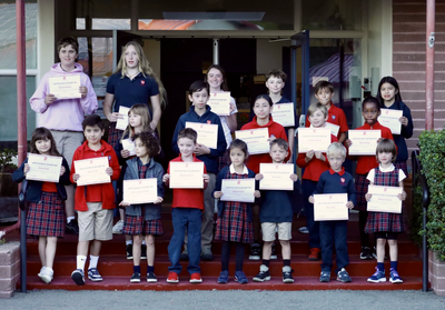 Group of children holding certificates in front of a building.