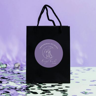 black gift bag with purple sticker and purple confetti around it