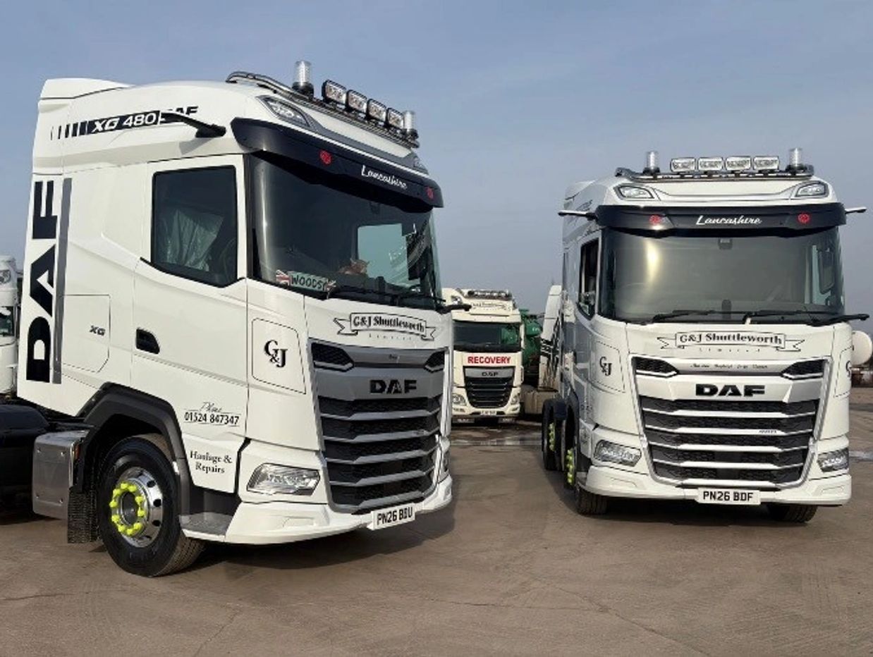 Two white DAF trucks parked side by side with company branding.