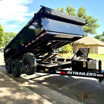 A black PJ dump trailer attached to a vehicle on a sunny street.