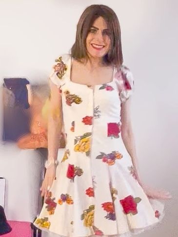 Smiling woman in a white floral dress posing indoors.