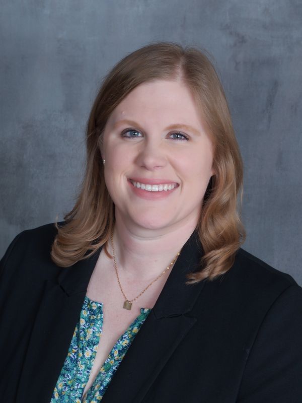 Professional woman smiling in a headshot with a floral blouse and black blazer. Taylor Lawrence Lashley.