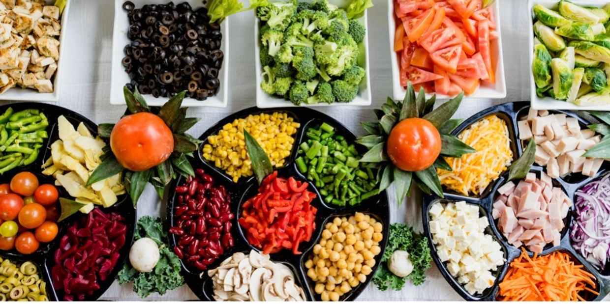 Colorful fresh vegetables and toppings arranged in trays for a salad bar.