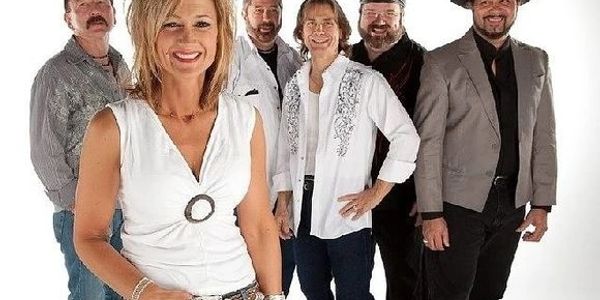 A smiling woman stands in front of five men in casual and semi-formal attire.