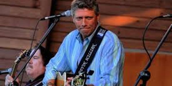 Man playing guitar and singing on stage with microphone.