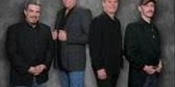 Four men posing against a gray backdrop, dressed in dark casual and semi-formal clothes.