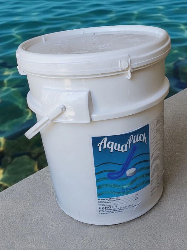 White bucket labeled AquaPuck near water edge.