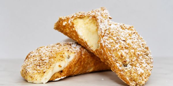 Two cannoli pastries filled with creamy ricotta and dusted with powdered sugar.