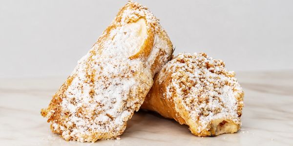 Two powdered sugar-coated cannoli pastries on a marble surface.