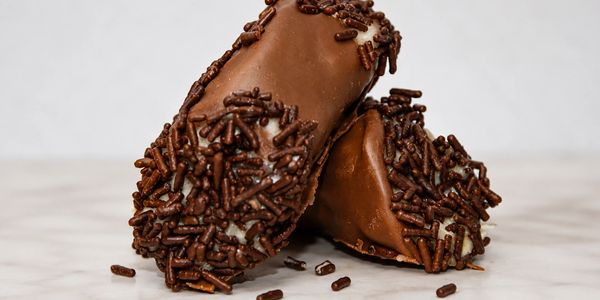 Two chocolate-covered treats with chocolate sprinkles on a marble surface.