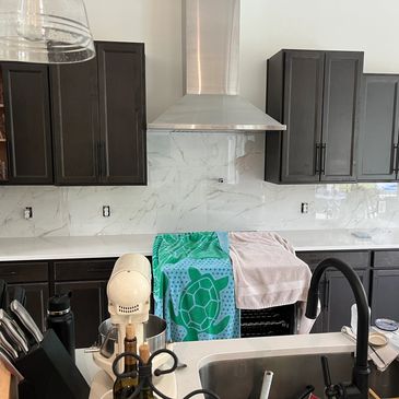 Modern kitchen with dark cabinets, white countertops, and a turtle-patterned towel.