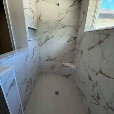 Modern shower with marble-patterned tiles and a small built-in bench.
