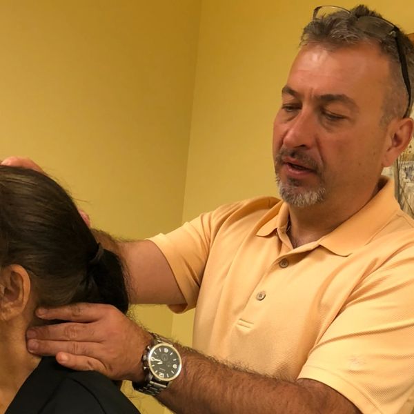 A man in a peach polo shirt examines a woman's neck indoors.