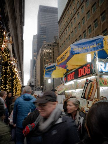 Busy street scene with a hot dog stand and festive lights in an urban area.