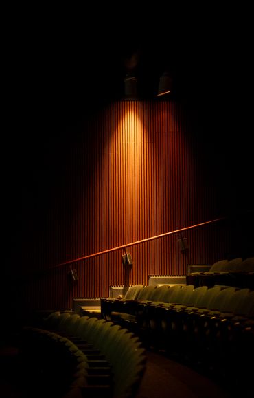 Dimly lit theater seats with warm spotlight on wooden wall.