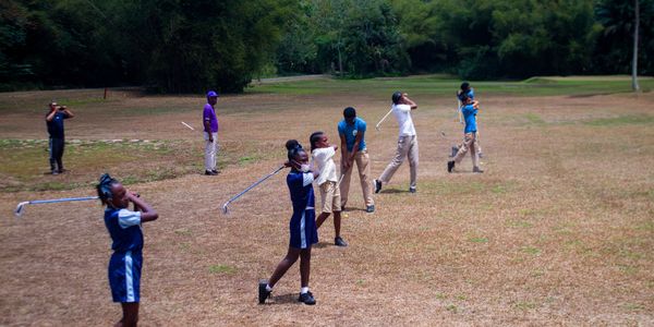 Children practicing golf swings on a grassy field with coaches watching.