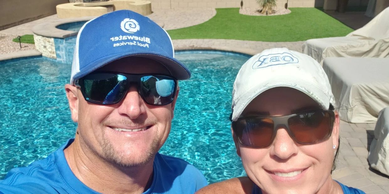 Two people wearing hats and sunglasses by a clear blue swimming pool.