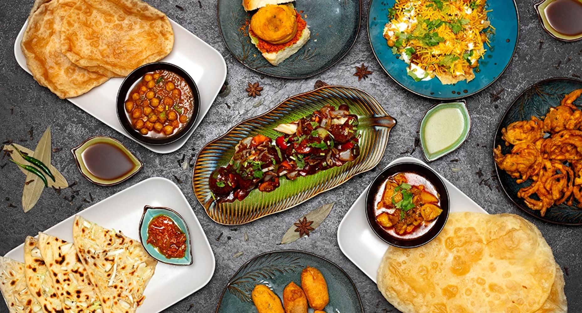 Assorted Indian dishes with breads, curries, and chutneys on a textured surface.