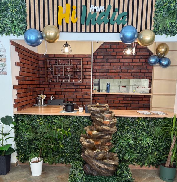 Reception area with a green plant wall and a water fountain under a 'Hi from India' sign.
