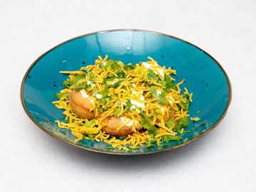 Indian snack topped with sev, yogurt, and fresh cilantro in a blue bowl.