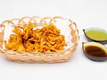 Basket of crispy pakoras with green chutney and tamarind sauce.