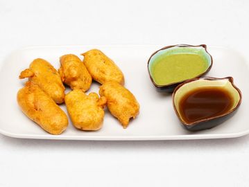 Plate of golden fried fritters served with green chutney and tamarind sauce.