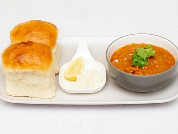 Pav bhaji served with two buns, chopped onions, and lemon wedge on a white plate.