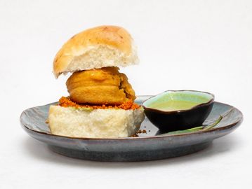 Indian snack vada pav served with green chutney on a ceramic plate.