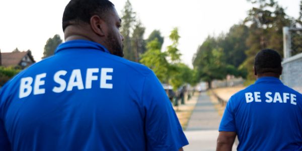 Two men in blue shirts with 'BE SAFE' text on back.