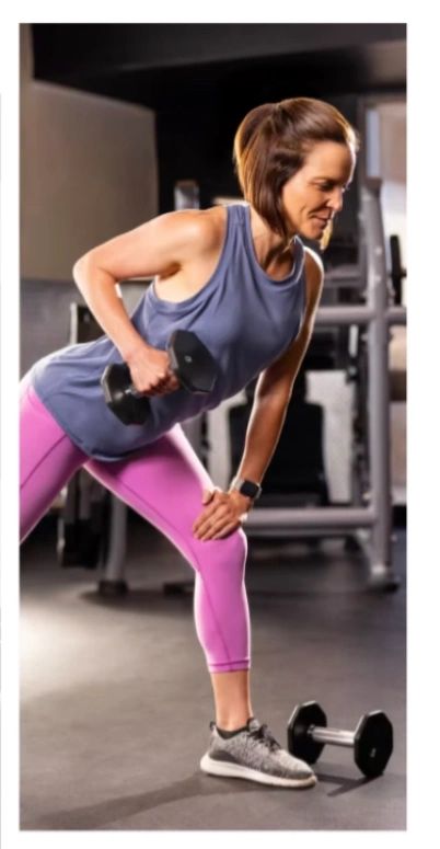 Woman in workout clothes lifting a dumbbell in gym.